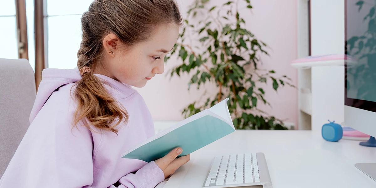 girl reading her notebook with computer in front of her