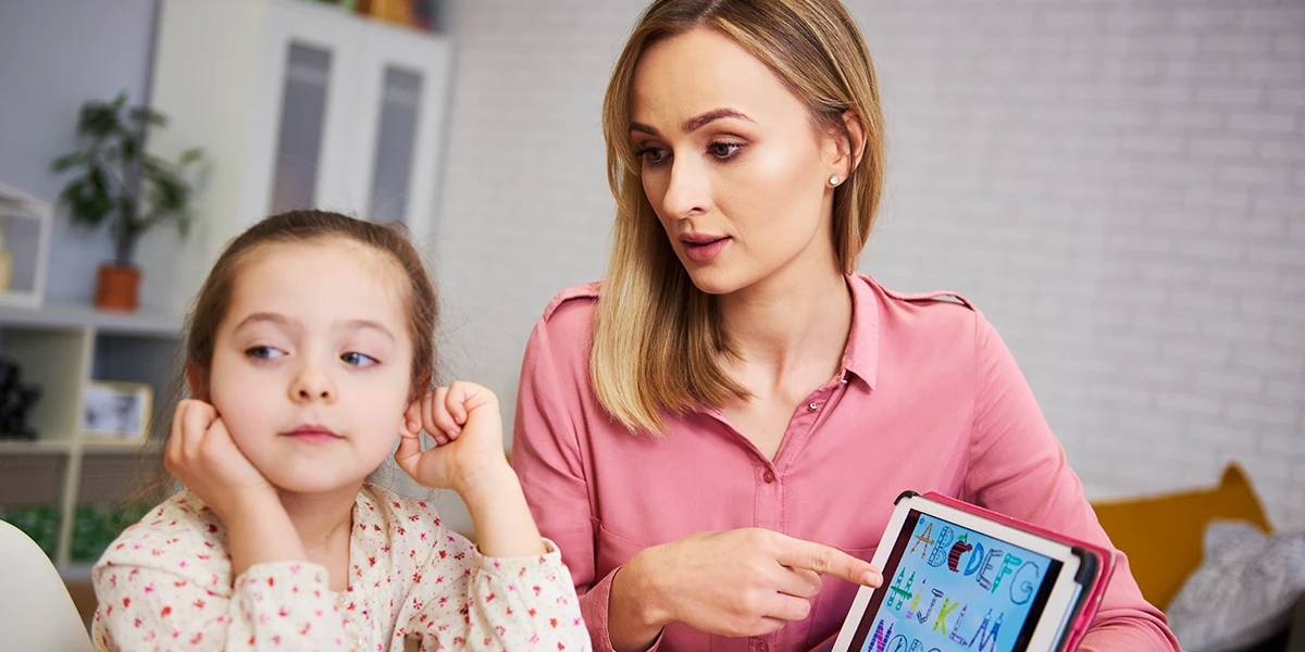 Mother trying to teach a little girl the alphabet using a tablet, but the girl doesn’t listen or pay attention. She doesn't know how to discipline a child that won't listen