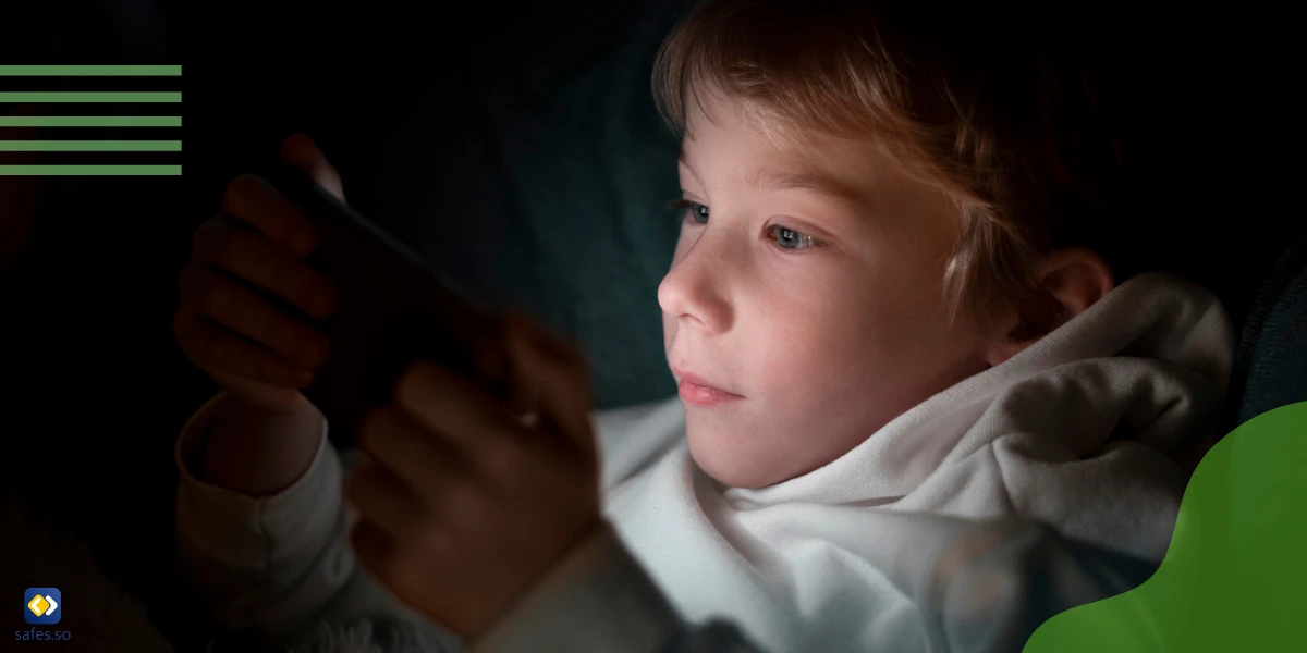 Little boy is looking at phone screen in bed