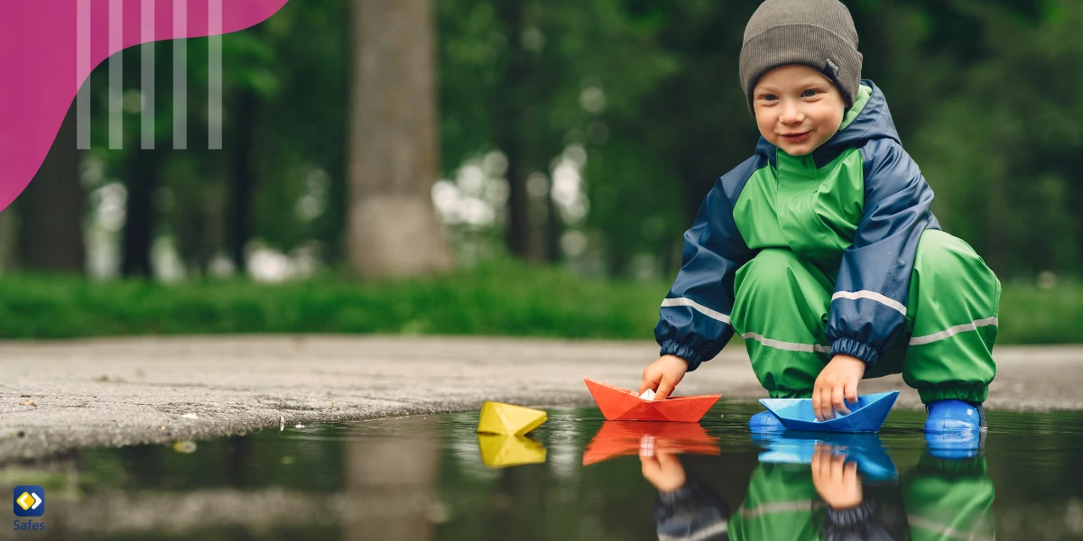 Little boy putting origami boats in a puddle