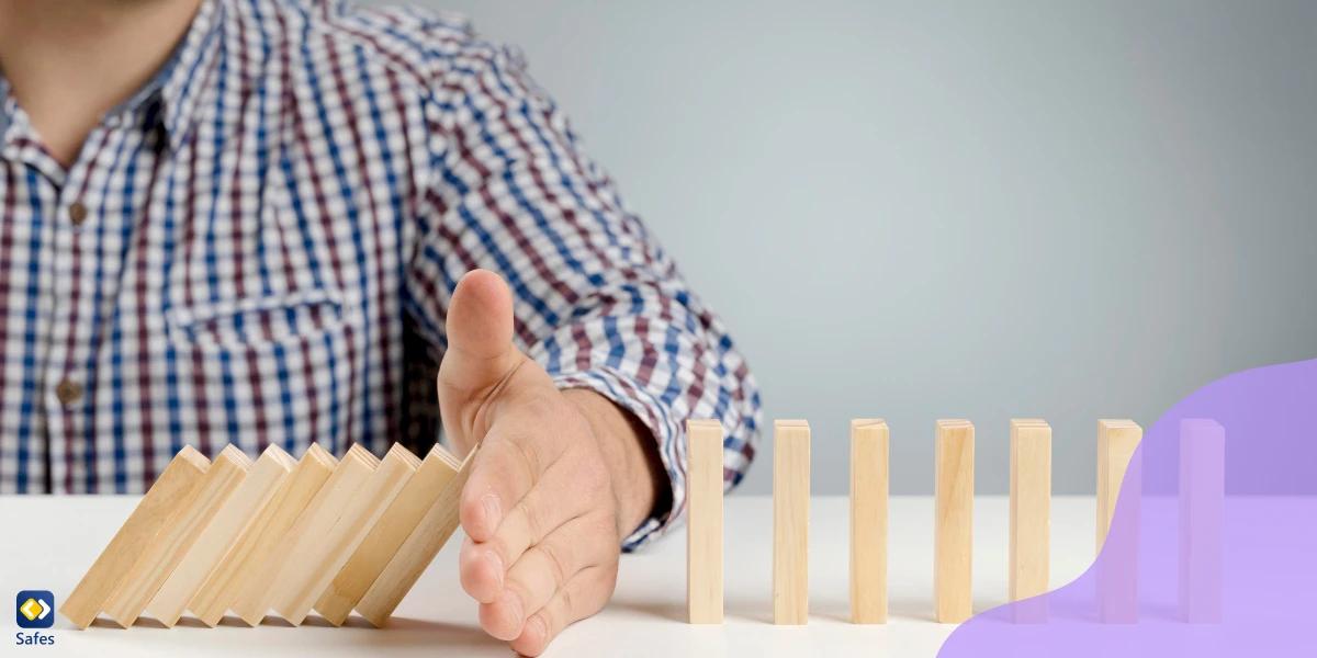 A symbolic picture showing the hand of a man stopping the dominos from falling