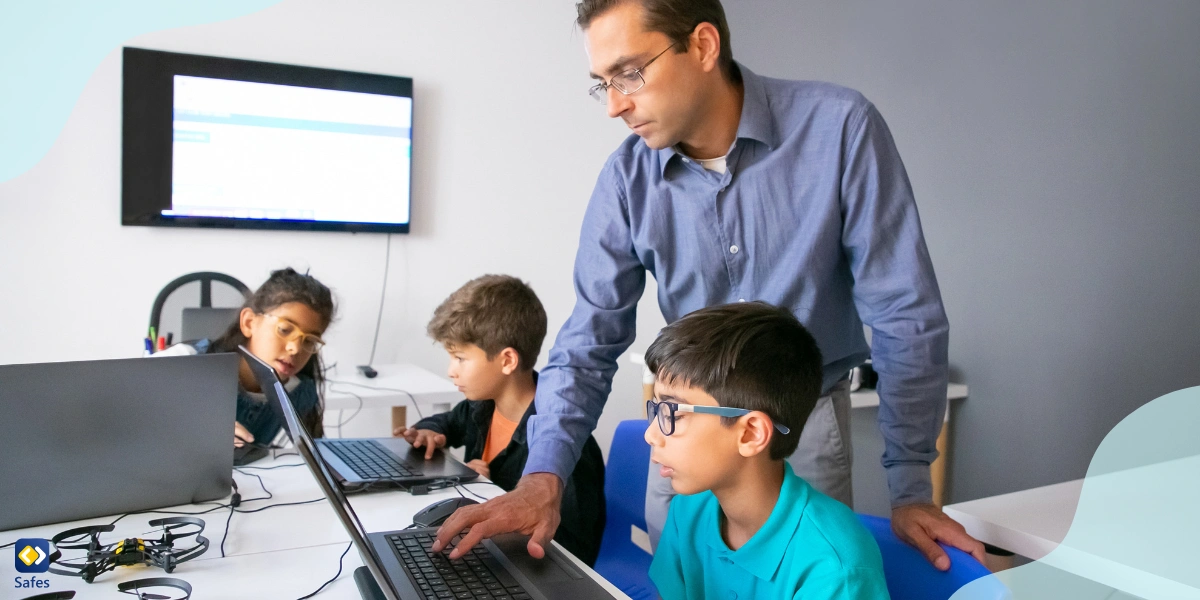Kinder arbeiten an Laptops und werden von einem Lehrer überwacht