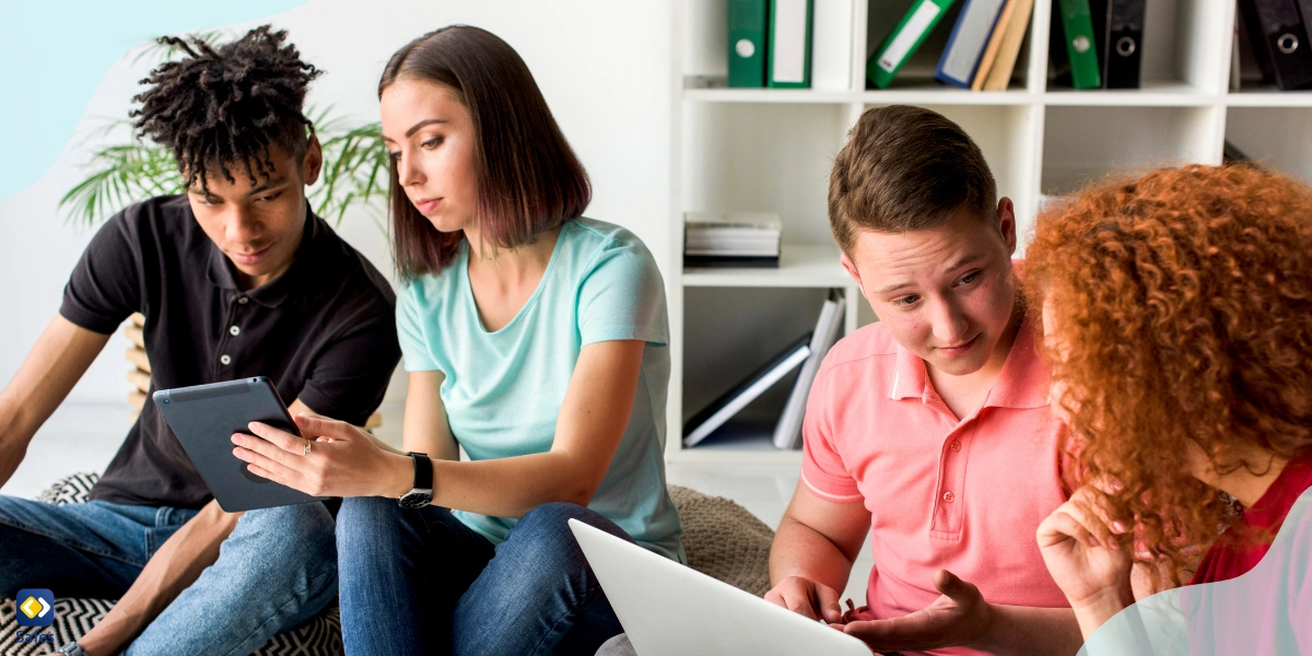 four students working on a group project, two are working on a laptop while the other two are using a tablet