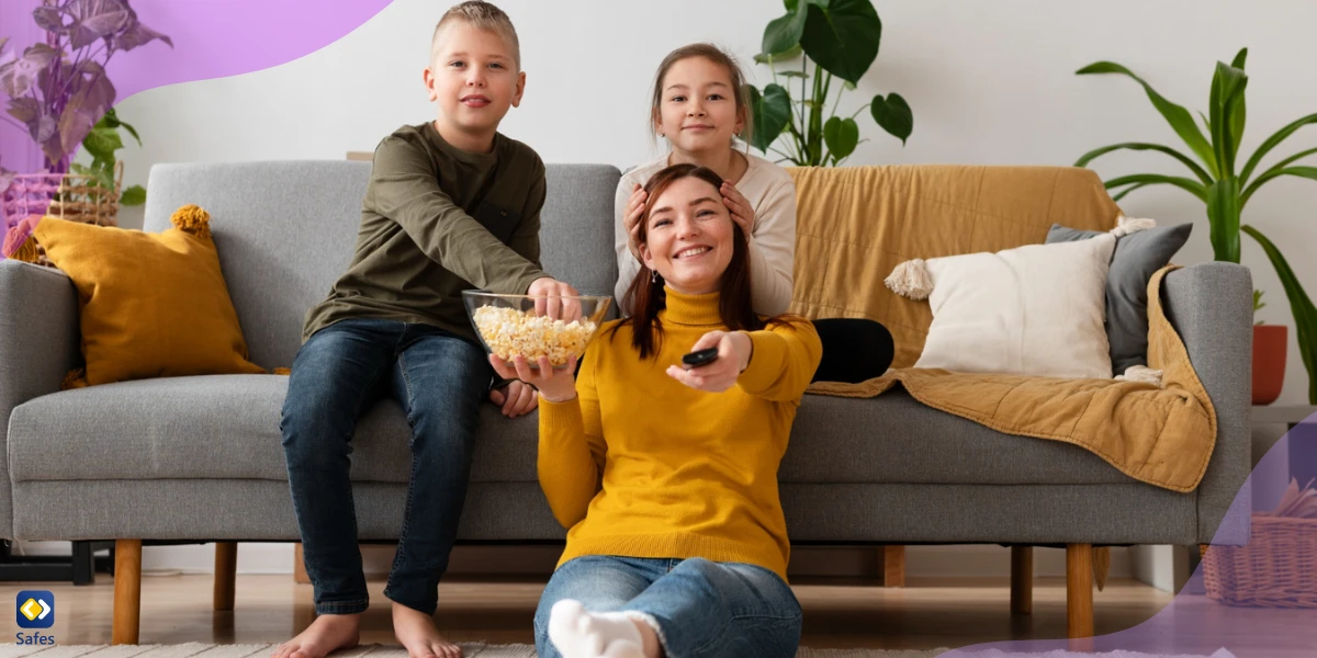 Mutter und kleiner Junge und Mädchen schauen zusammen auf einem Sofa fern und essen Popcorn