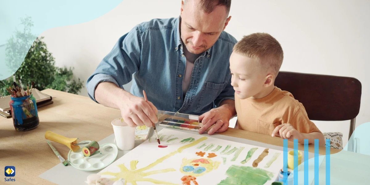 Vater hilft seinem kleinen Sohn mit Pinsel und Farben, am Tisch ein Bild auf Papier zu malen