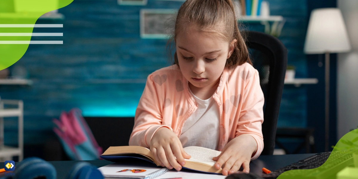 A little girl is sitting at a desk looking at a book