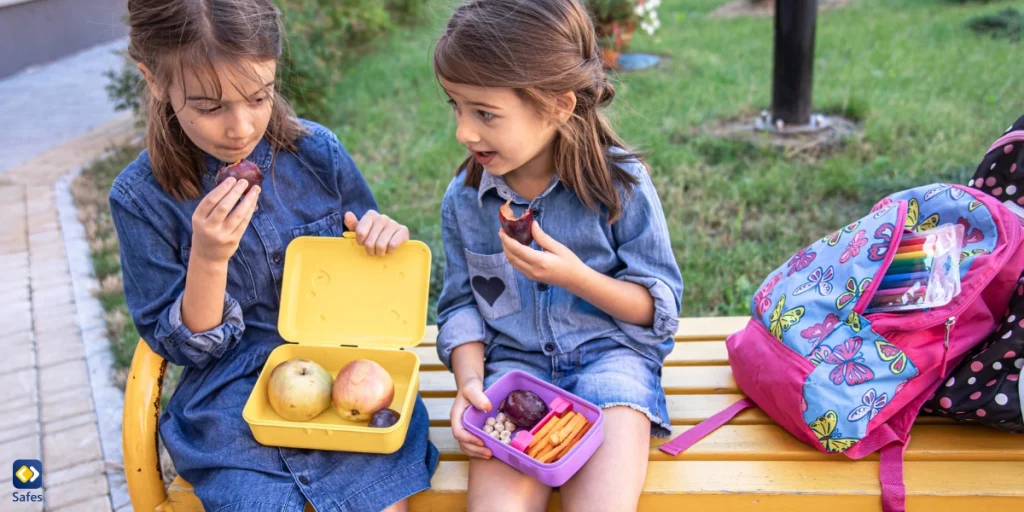 two girls eating fruit from their lunch boxes