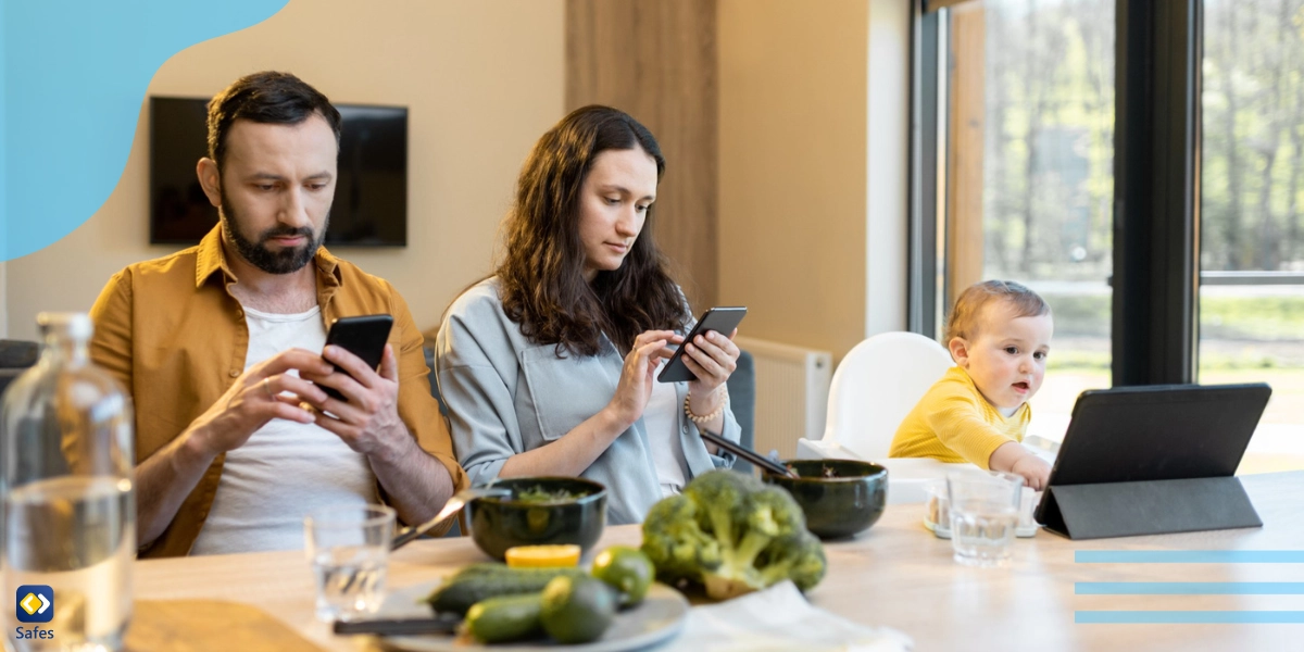dreiköpfige Familie sitzt an einem Tisch mit Essen, aber sogar das Baby benutzt ein technisches Gerät