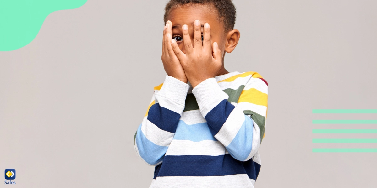 Little boy covers his face with hands while looking out with one eye