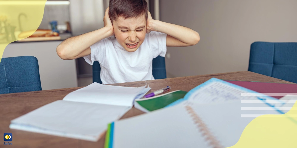 boy being overwhelmed with hands over his ears and books in front of him.