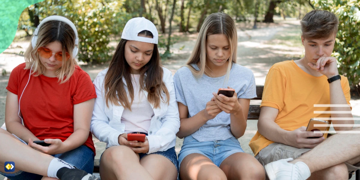 Four teenagers sitting on a bench, texting on their mobile phones. They’re probably using teen lingo slang terms such as rizz.
