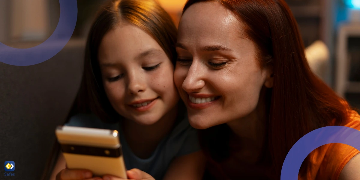 A mother and a daughter looking smiling and looking at a smartphone.