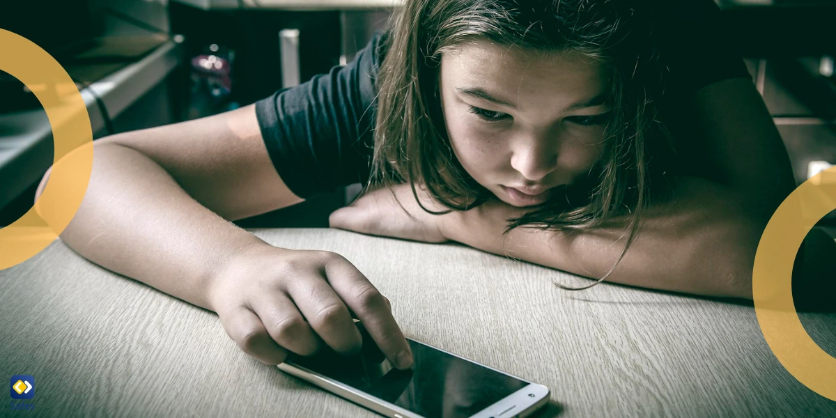 sad young girl slouching on table with a smartphone in front of her and one finger resting on the screen.