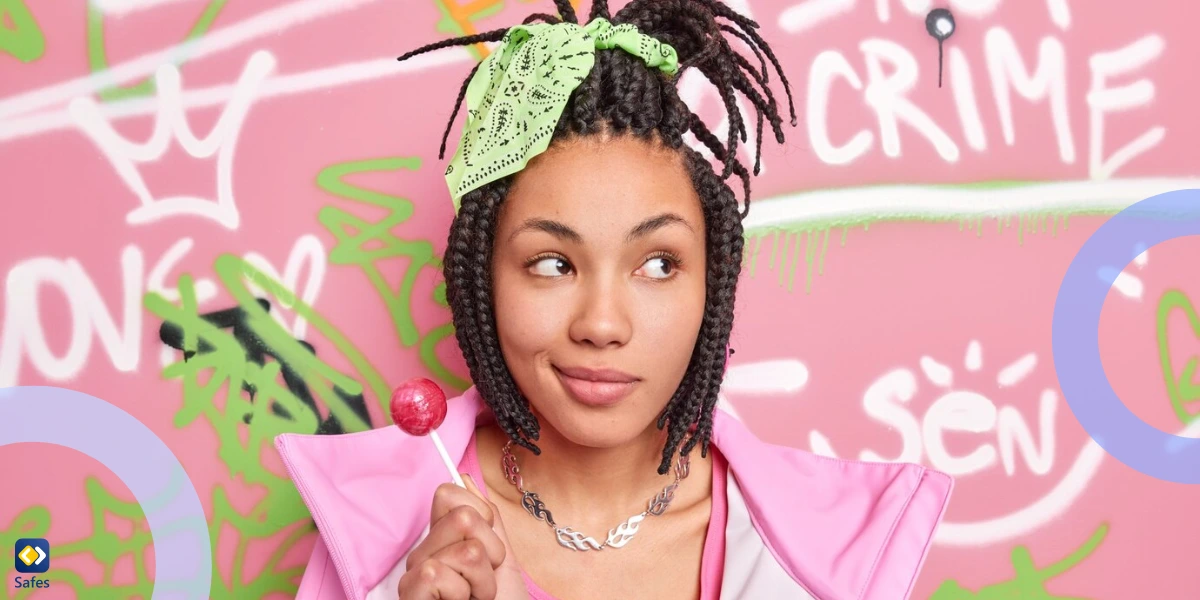 Teen girl with braids and green bandana holds a lollipop, standing playfully in front of colorful pink graffiti wall.
