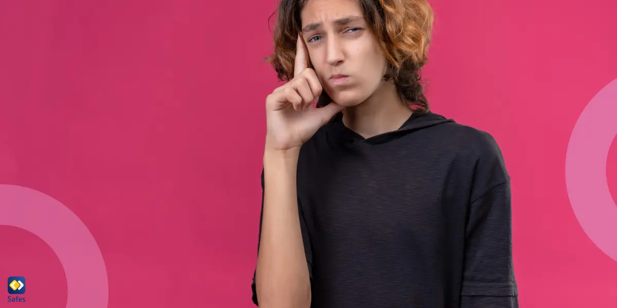 A teen with long, wavy hair and a black t-shirt stands against a pink background, looking thoughtfully ahead with one finger resting on their cheek in a skeptical or disapproving expression.