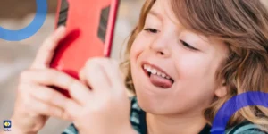 A kid using a mobile phone while making a goofy face.